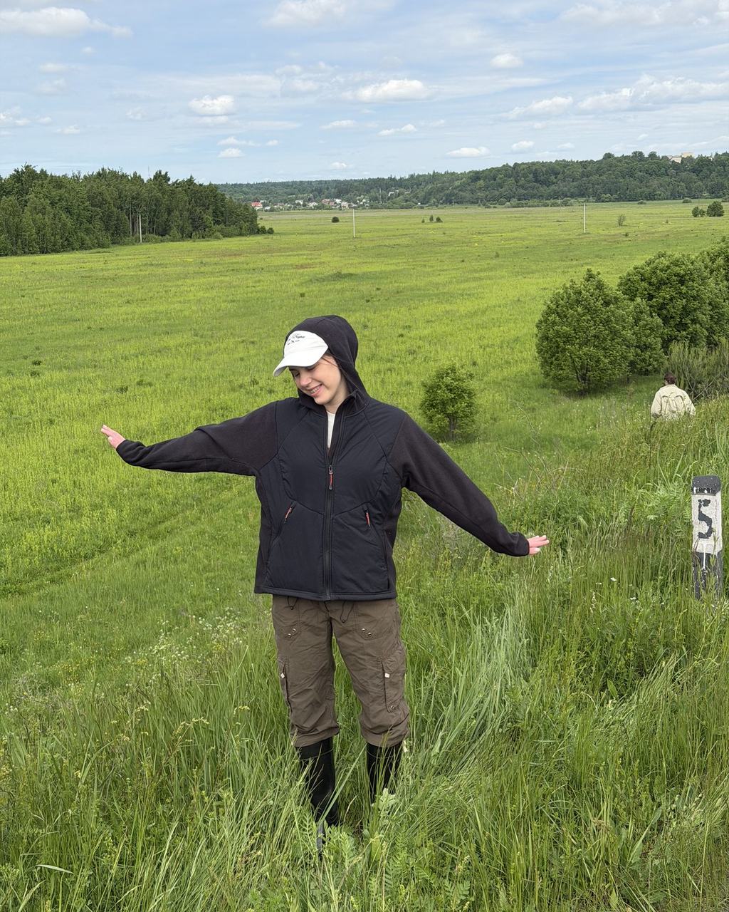 Mariia Miroshnik standing in an open meadow near a forest treeline